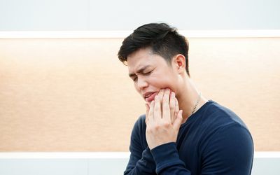 close up adult asian man using hand massage cheek cause from toothache wisdom tooth at house dental health care concept 1128034562 5c8aa82846e0fb0001f8cfd5