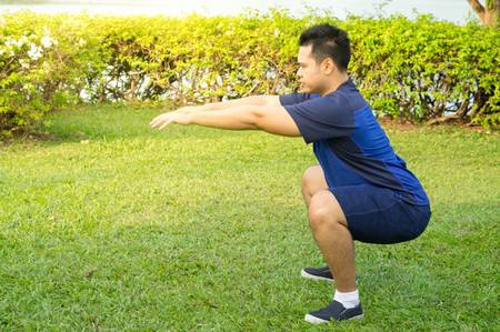 107196649 asian man doing squat exercise in park