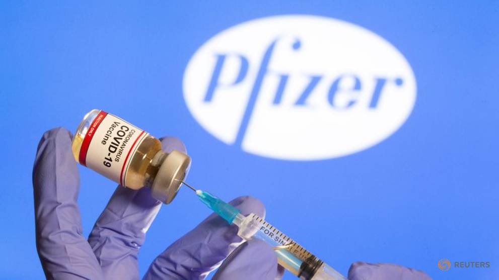 file photo a woman holds a small bottle labeled with a quot coronavirus covid 19 vaccine quot sticker and a medical syringe in front of displayed pfizer logo in this illustration 1