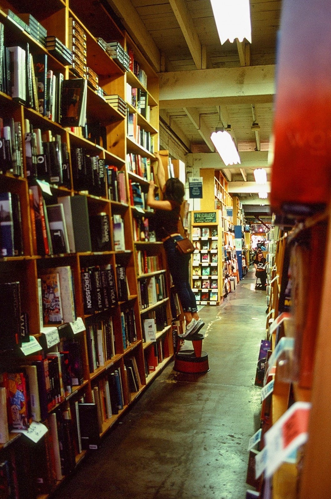 Woman on her tip toe at bookstore trying to take a book at the top shelf