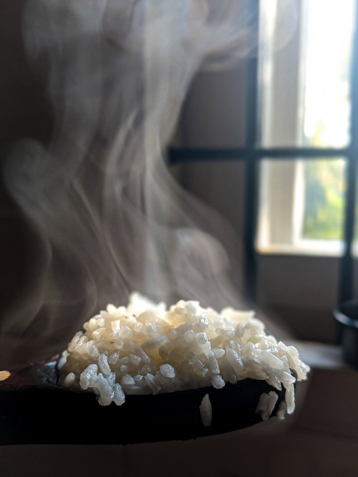 steaming hot white rice on a spoon next to a window