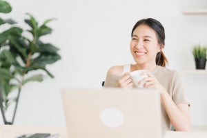 beautiful young smiling asian woman working laptop drinking coffee