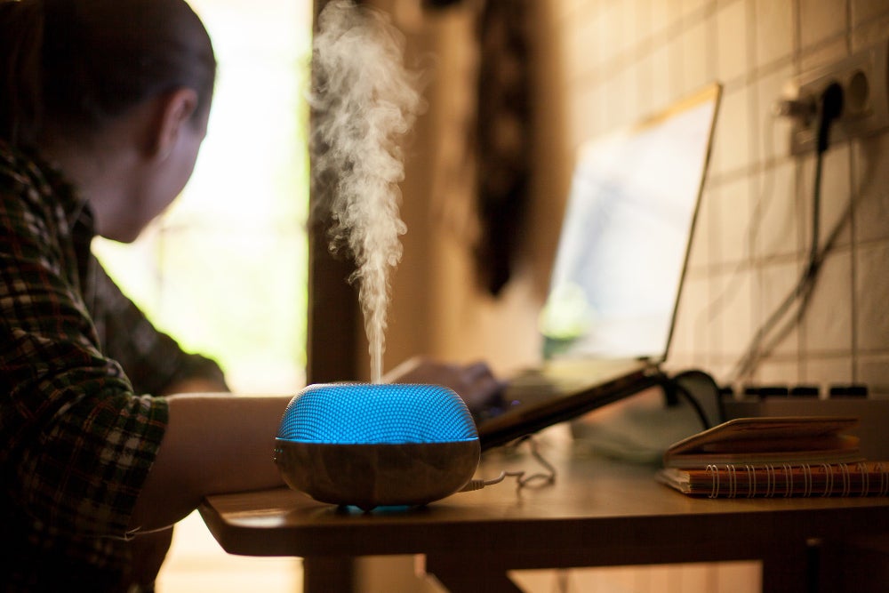 vapor coming out from essential oil diffureser with blue led while woman working laptop