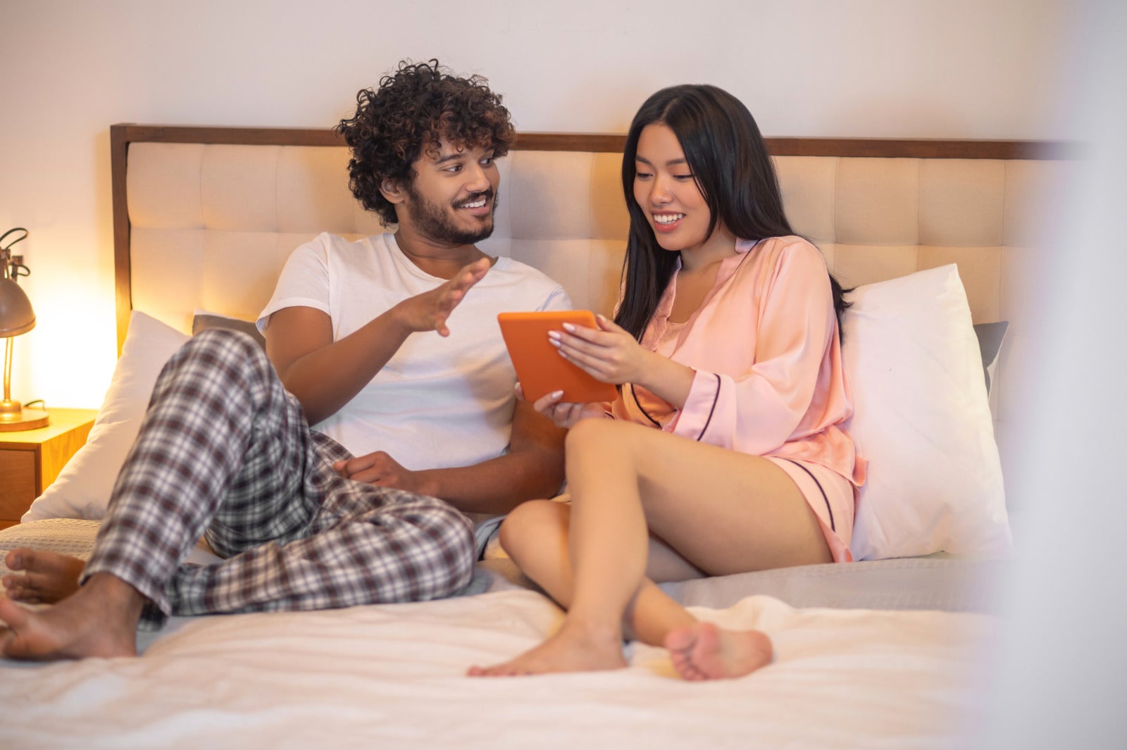 man looking woman with tablet lying bed