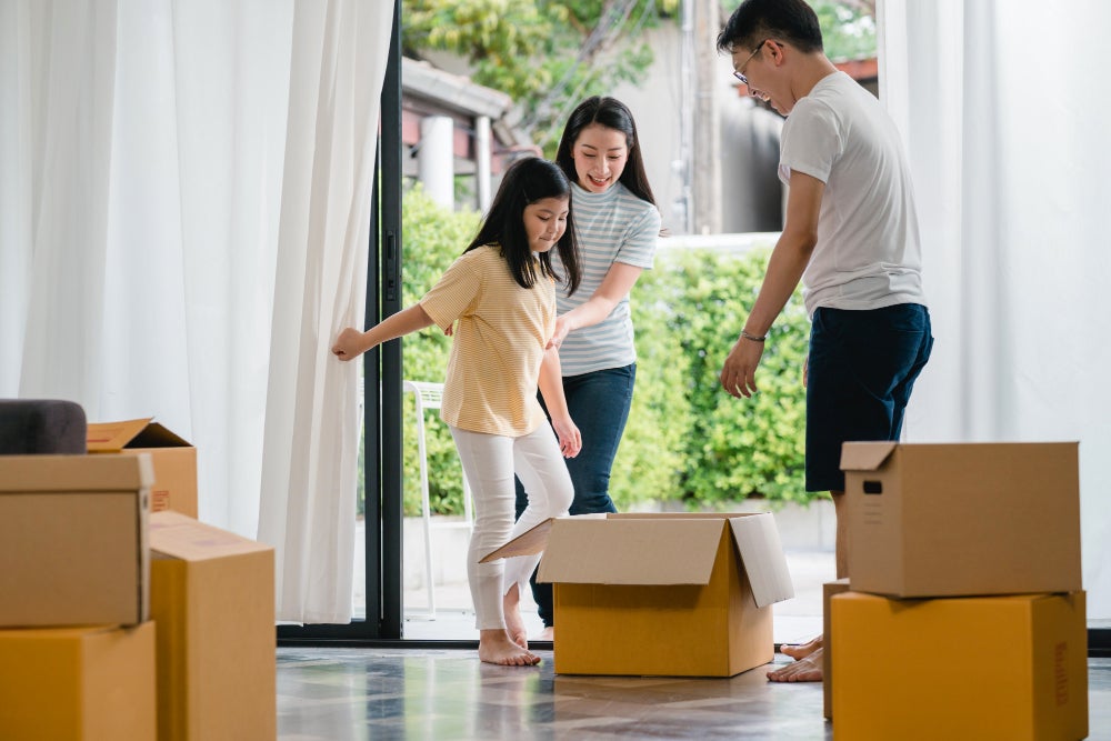 happy asian young family having fun laughing moving into new home japanese parents mother father smiling helping excited little girl riding sitting cardboard box new property relocation 1