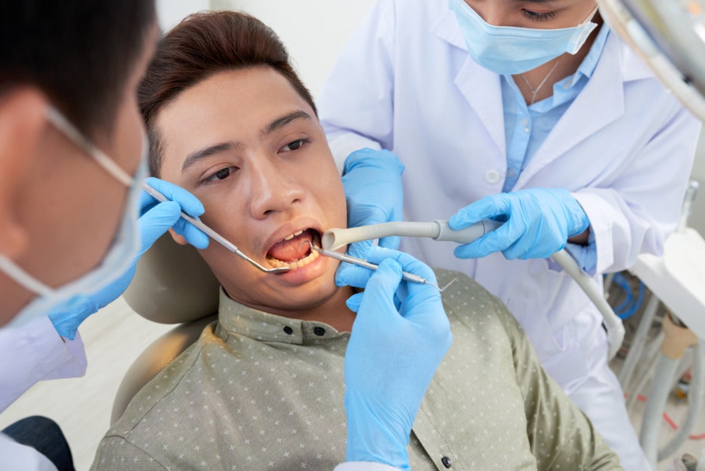 unrecognizable asian dentist nurse examining male patient s teeth