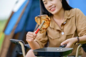 portrait portrait happy young asian woman camping alone grilled pork barbecue picnic pan cooking food while sitting chair camping site