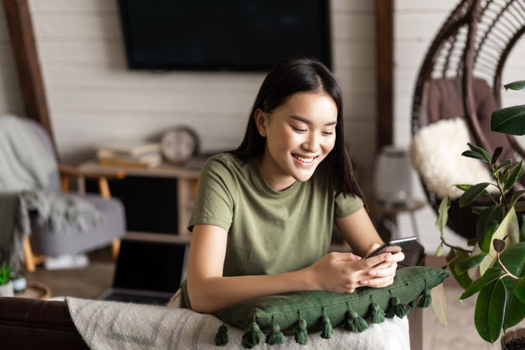 smiling korean girl chatting mobile phone sitting home living room with smartphone laug 1