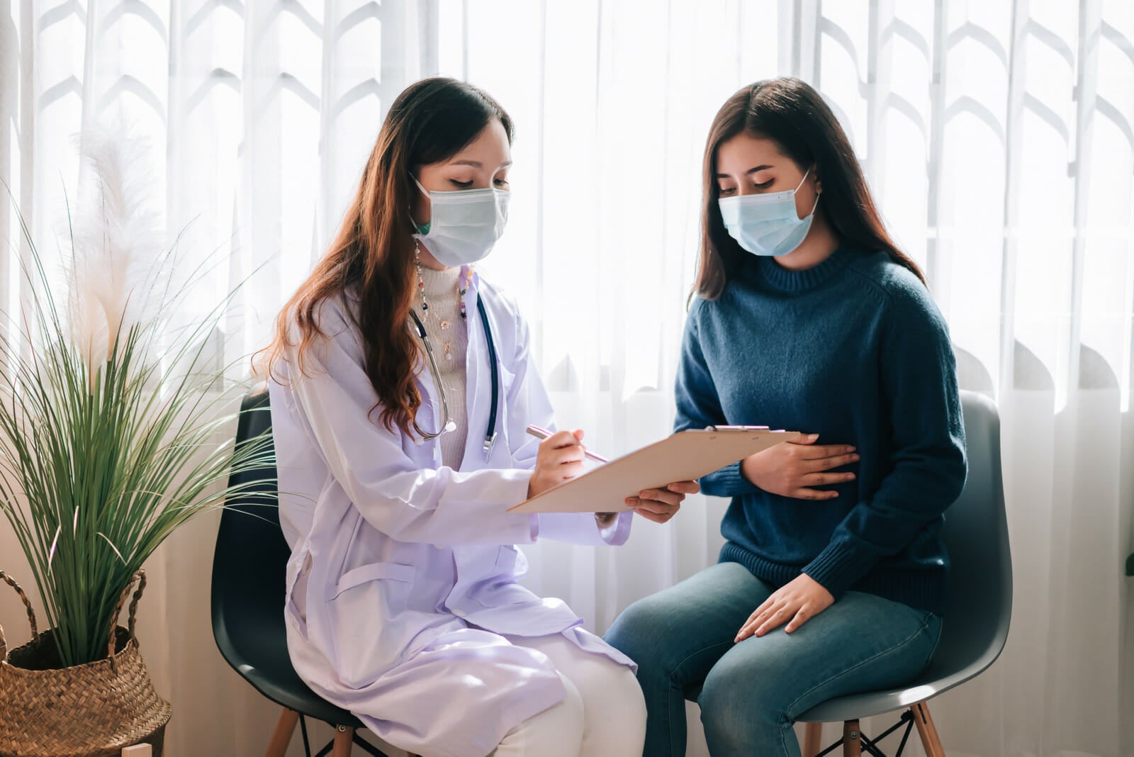 asian doctor visit examines young adult woman hospital with stomach ache doctor checking up consulting health care wearing mask protect covid19 pandemic