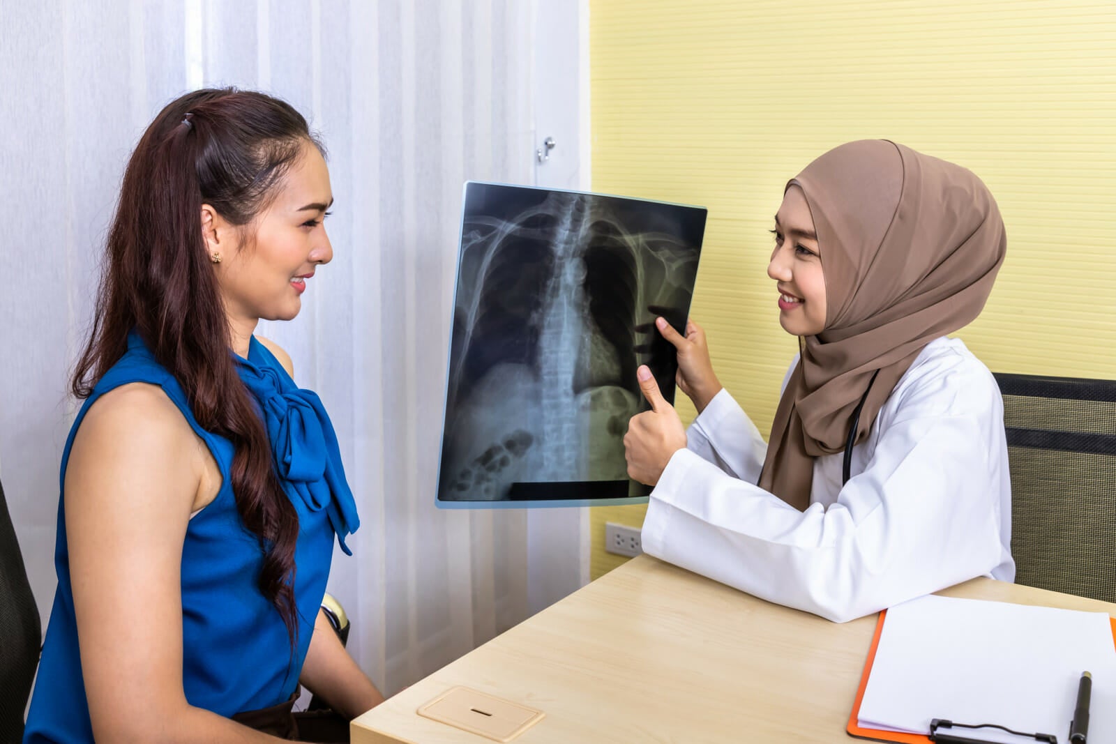 muslim female woman medical doctor examining looking pointing xray film giving explanation patient who sitting chair