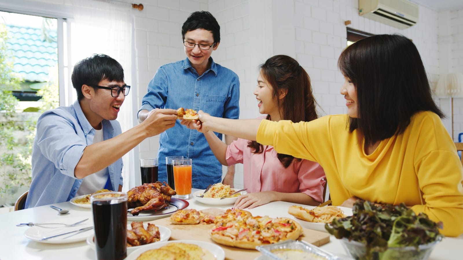 happy young friends group having lunch home asia family party eating pizza food laughing enjoying meal while sitting dining table together house celebration holiday togetherness
