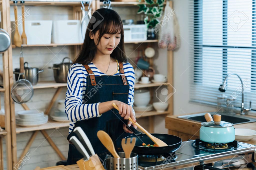 190943535 portrait of a pretty concentrated asian wife cooking with a frying pan by the gas stove at daytime