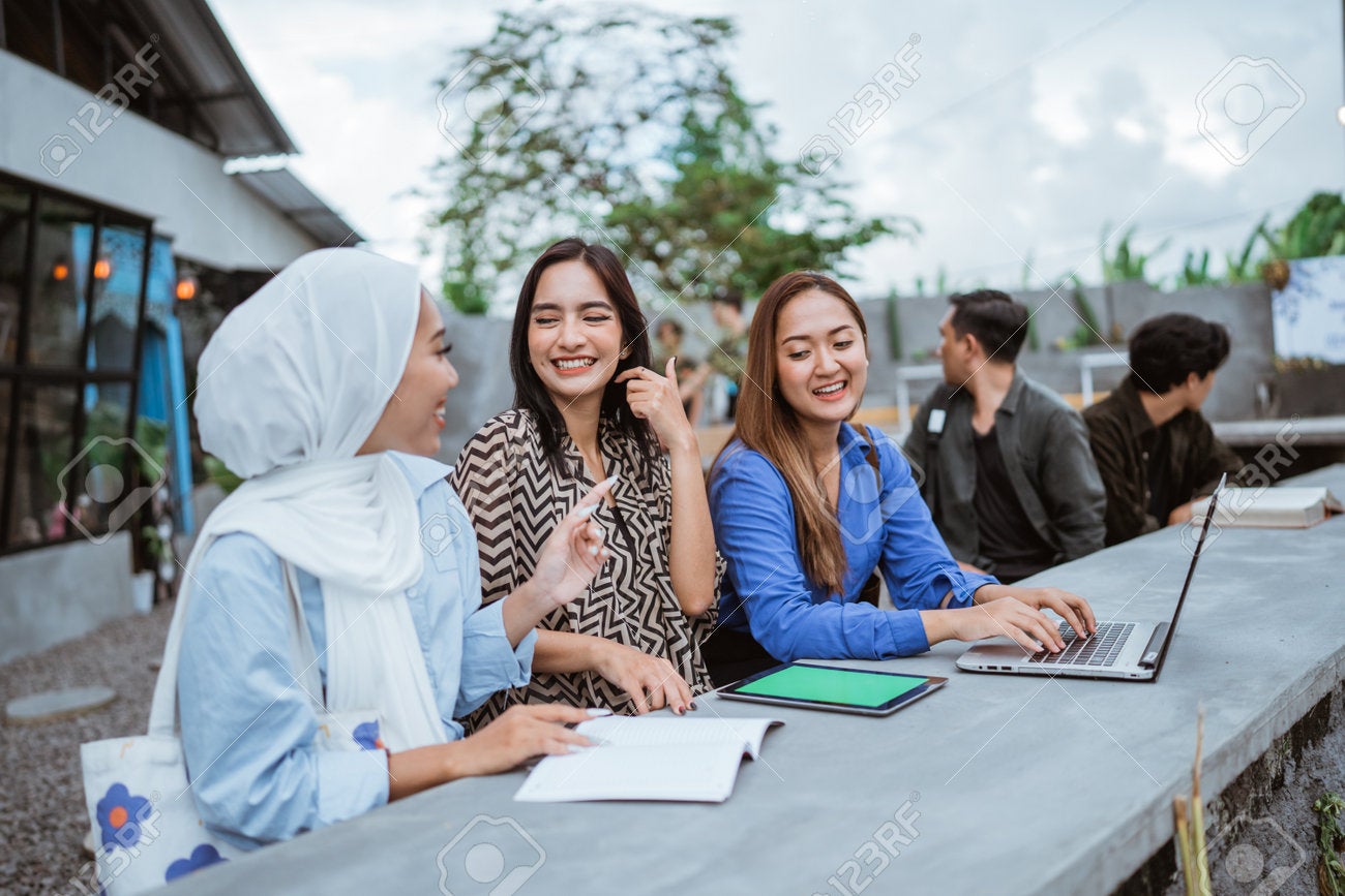 208620069 Three Asian Female Students Chat While Working On A Project Together In An Outdoor Coworking Space