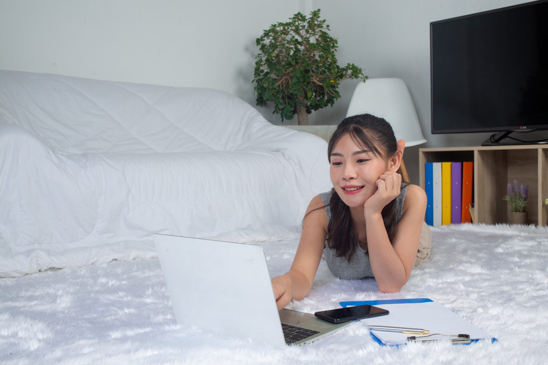 young woman is using laptop enjoy with her work while laying near sofa