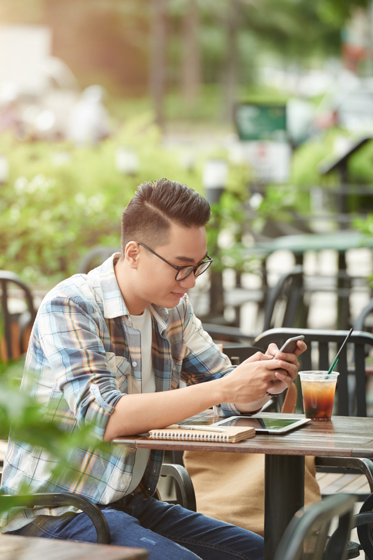 young asian male student sitting street cafe using smartphone